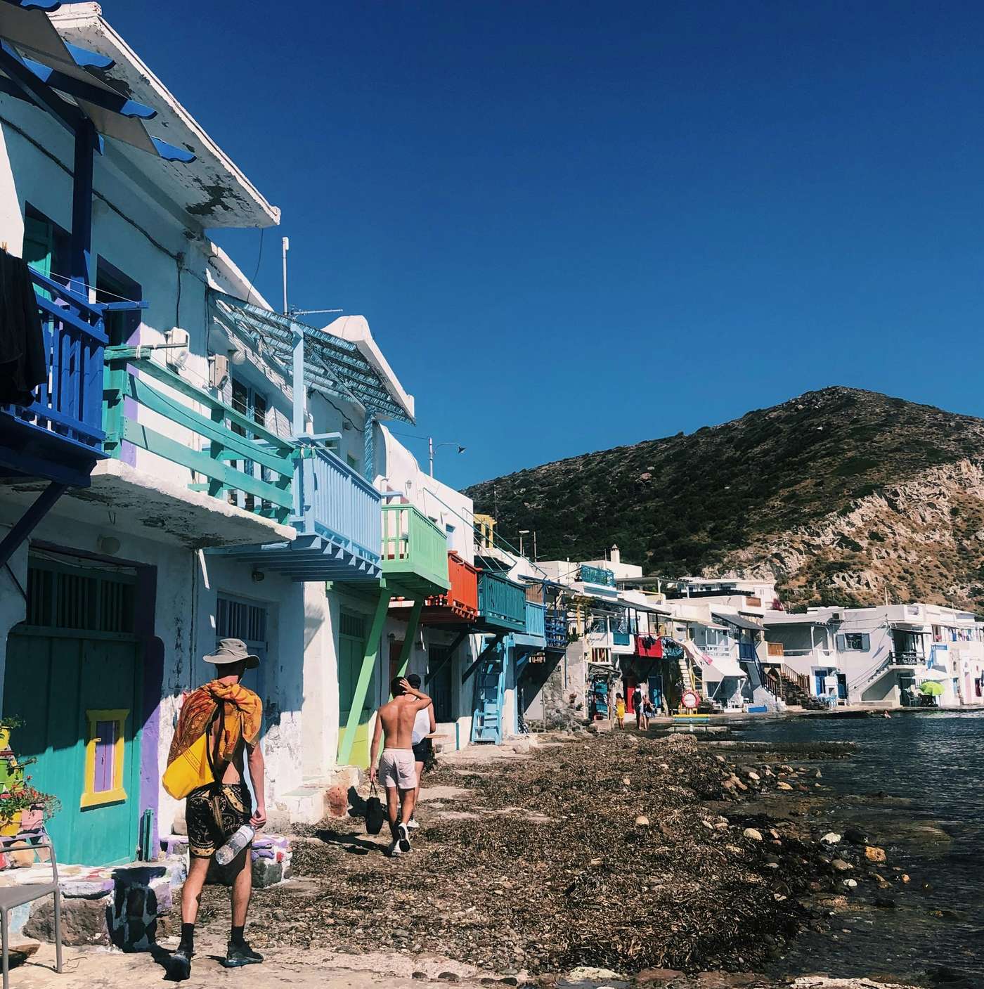 9990586 Vibrant bungalows line the seashore in Milos, Greece under a bright blue sky. Perfect travel destination.