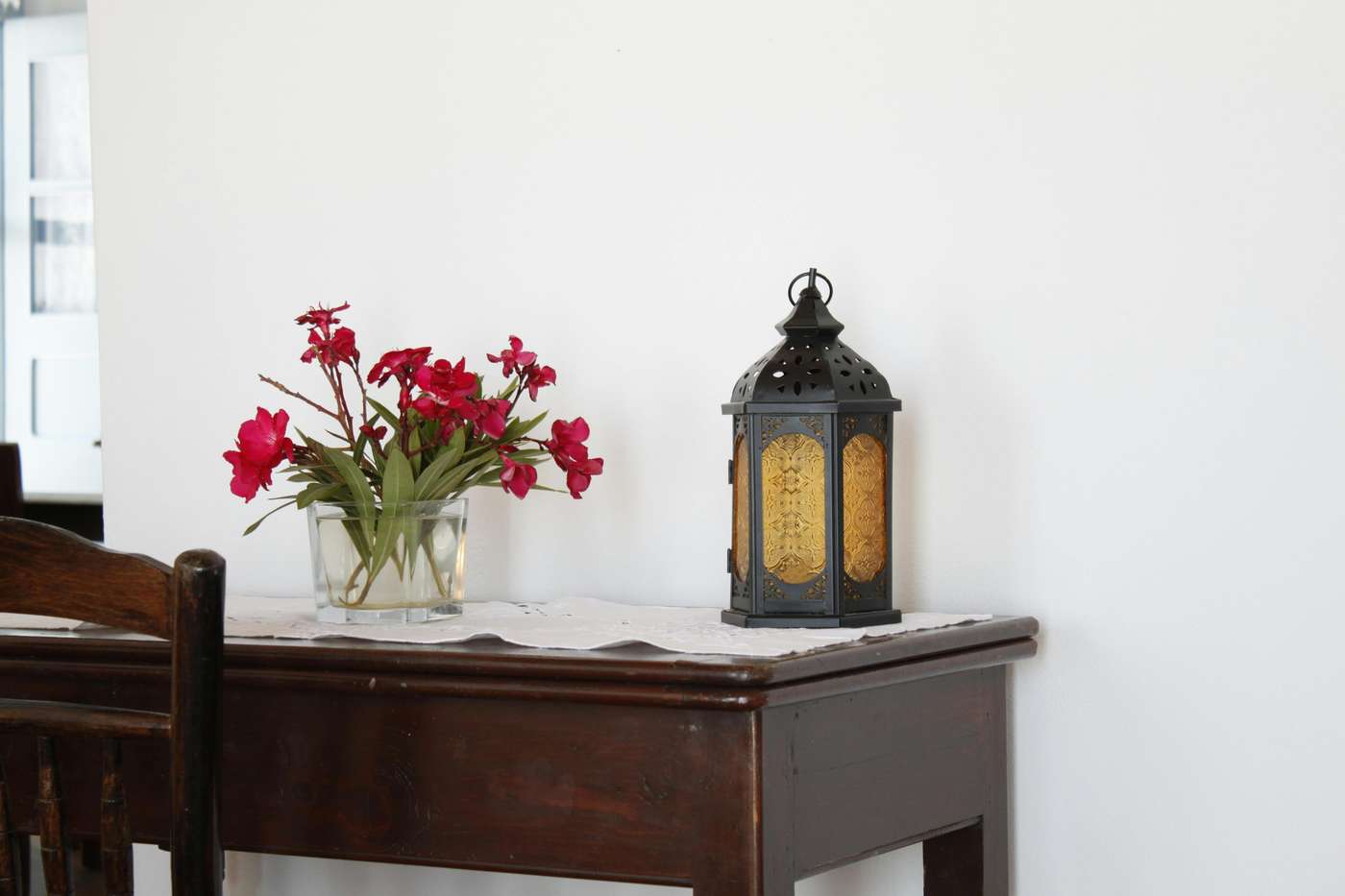 Charming table setting with red flowers and lantern, offering rustic elegance in Milos, Greece.