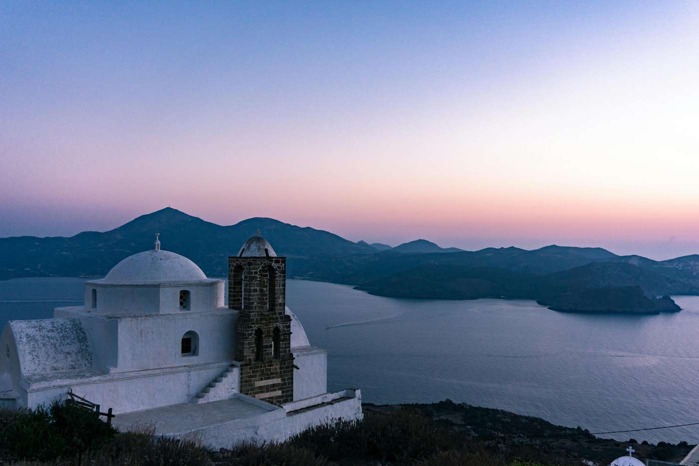 2734920 Captivating view of a white church in Milos, Greece, overlooking the serene ocean at sunset.