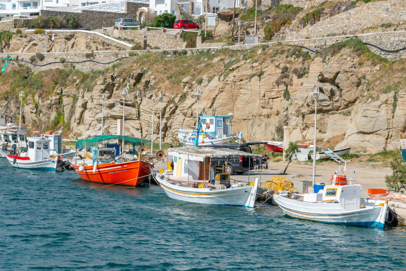 15241842 Vibrant fishing boats docked at a picturesque coastal area with rocky cliffs under a sunny sky.