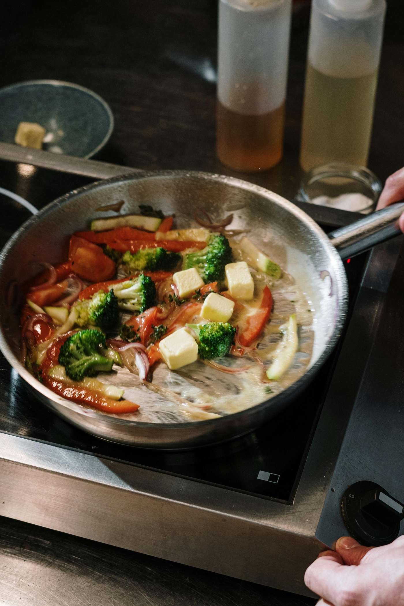 A chef cooks colorful vegetables in a skillet with butter on a stove in the kitchen.